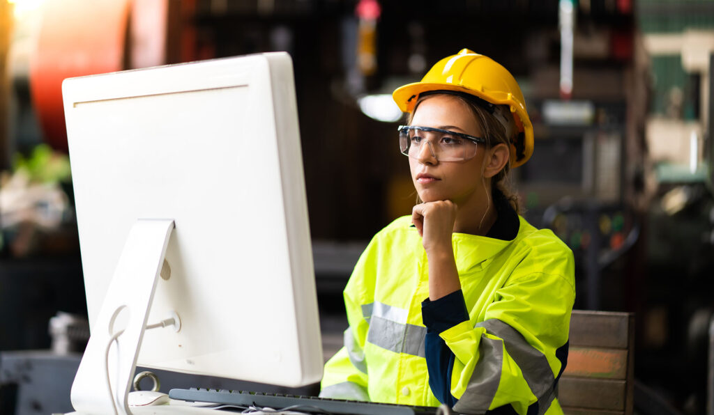A woman in a hard hat reviews training materials on a computer.