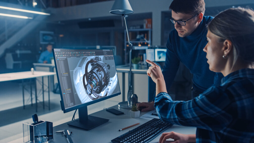 Two engineers working at a desktop review a model together.