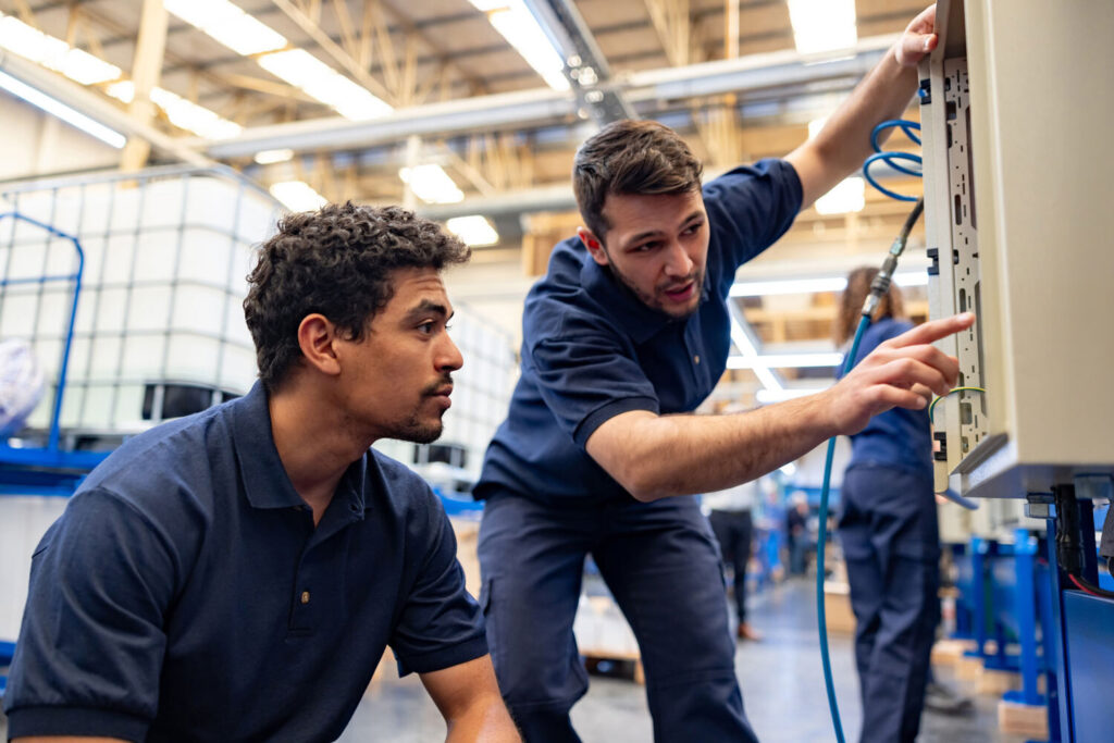 Two employees in a manufacutring warehouse examining an electrical box