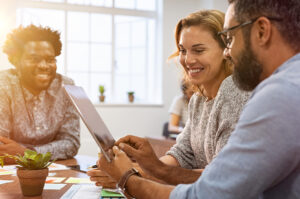 Successful business people discussing while using digital tablet in office. Multiethnic business team working on tablet in their company. Mature businessman showing data on screen to smiling woman.