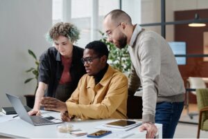 Three employees discuss information on a laptop screen.
